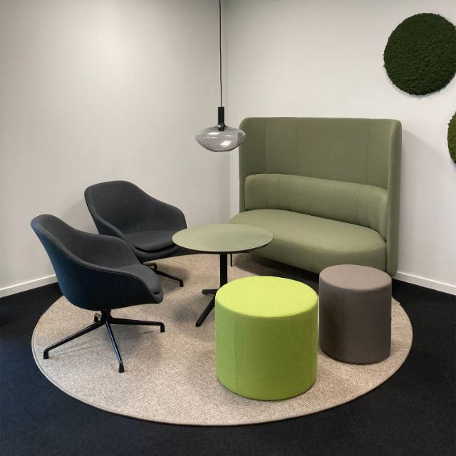 Loungeområde indrettet med sofa, lænestole og puf i naturlige farvenuancer for at skabe en hyggelig og hjemlig stemning på kontoret